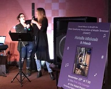 students singing next to a poster for the benefit concert